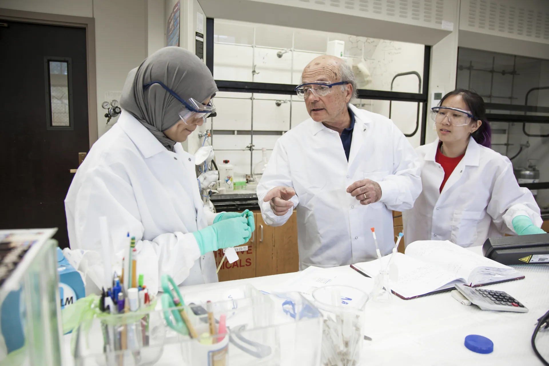 Three researchers in lab coats working together at a bench.